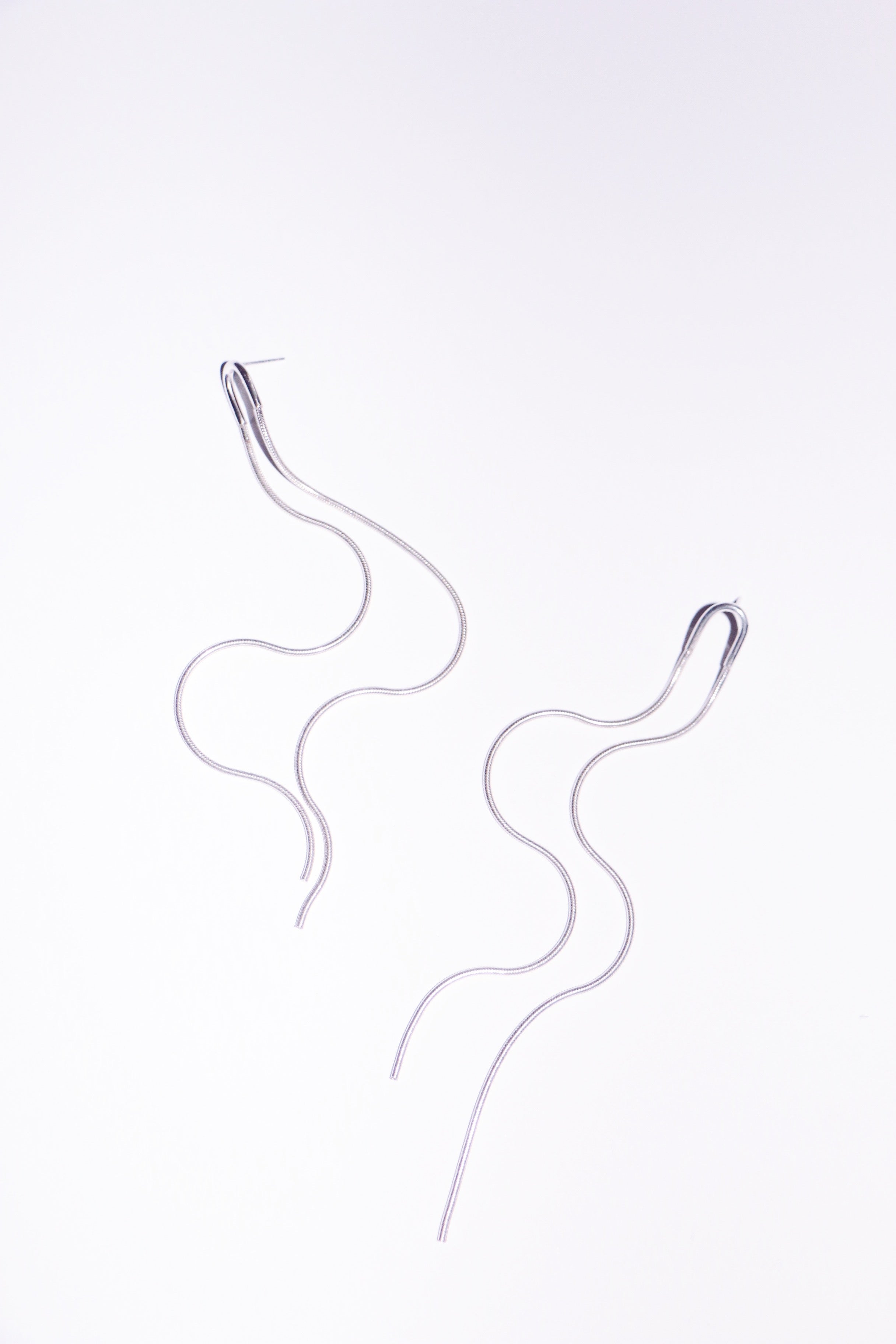 Image of a womans neck and part of her face, mouth and ear featuring a long chain ear cuff in silver.